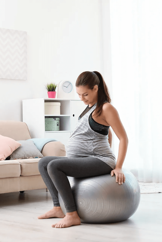 várandós nő egy nappaliban, fitball labdán ül