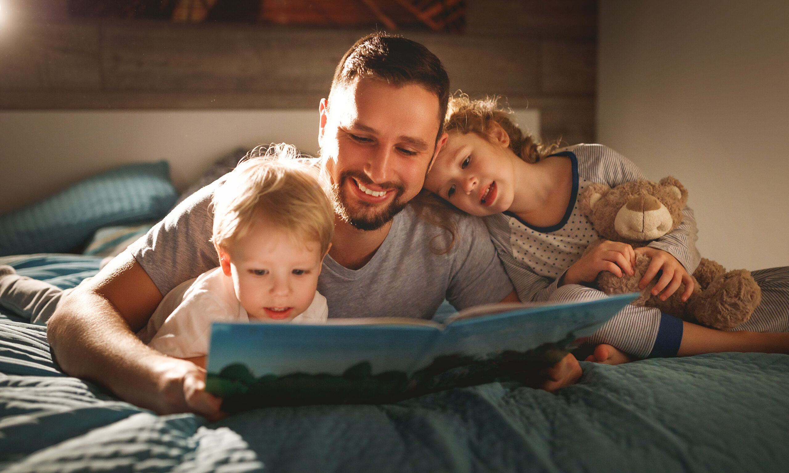 Apa könyvet olvas két lányának az ágyban hason fekve