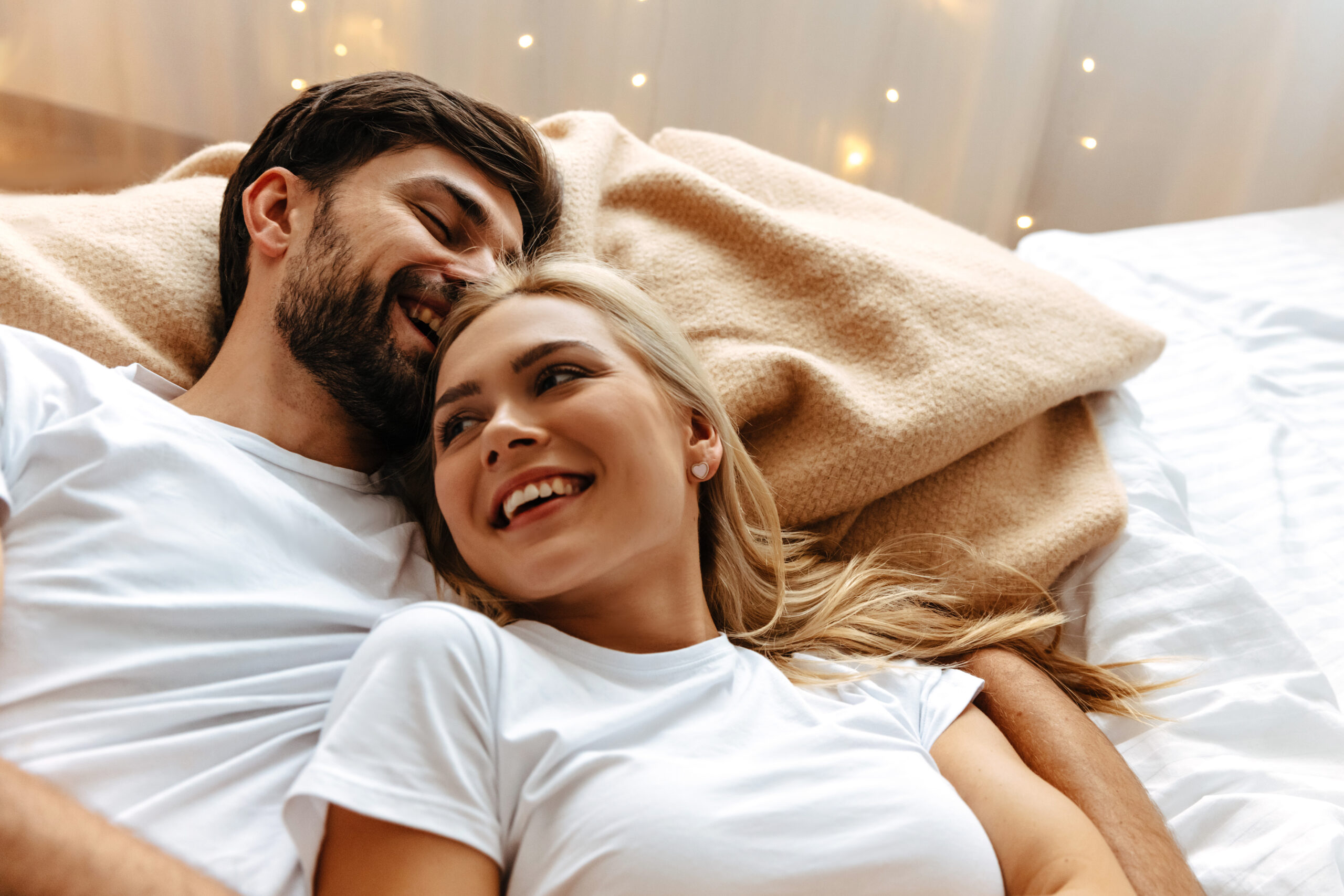fiatal pár az ágyban kedve, mindketten fehér pólóban, mosolyognak